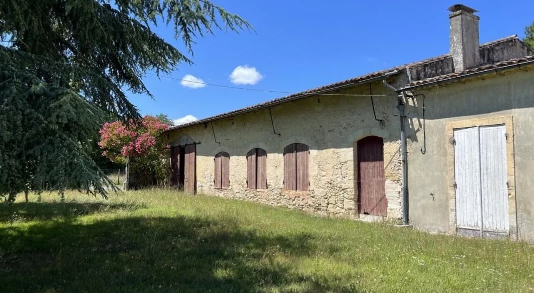Maison en pierre avec fenêtres et volets, entourée d'un jardin.