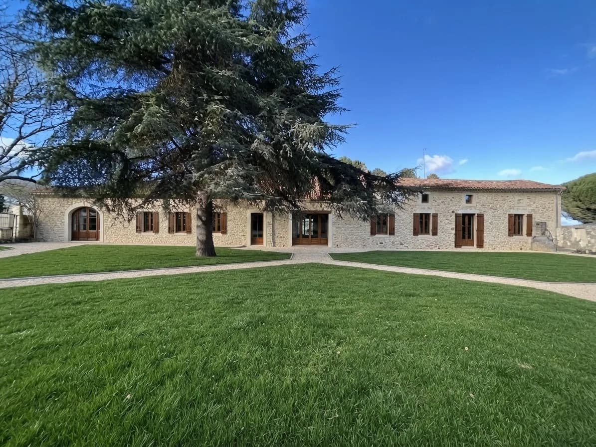 Maison en pierre avec jardin arboré et chemin en gravier.